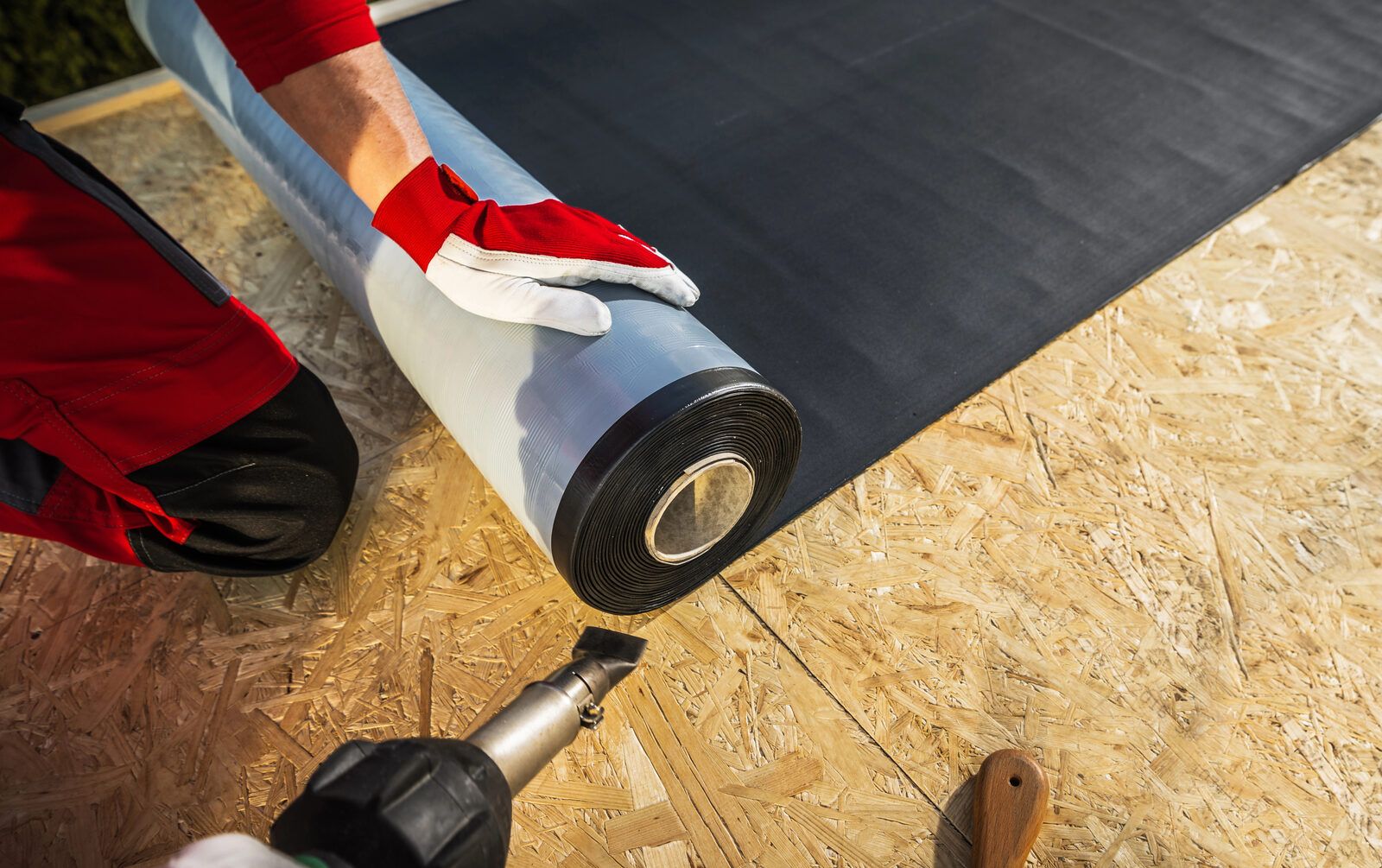 A roll of leak barrier membrane being pressed onto a plywood roof deck.