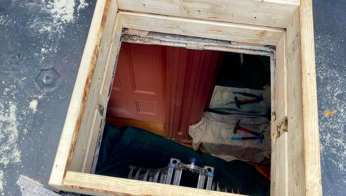 A framed opening cut into the roof membrane above a room below.